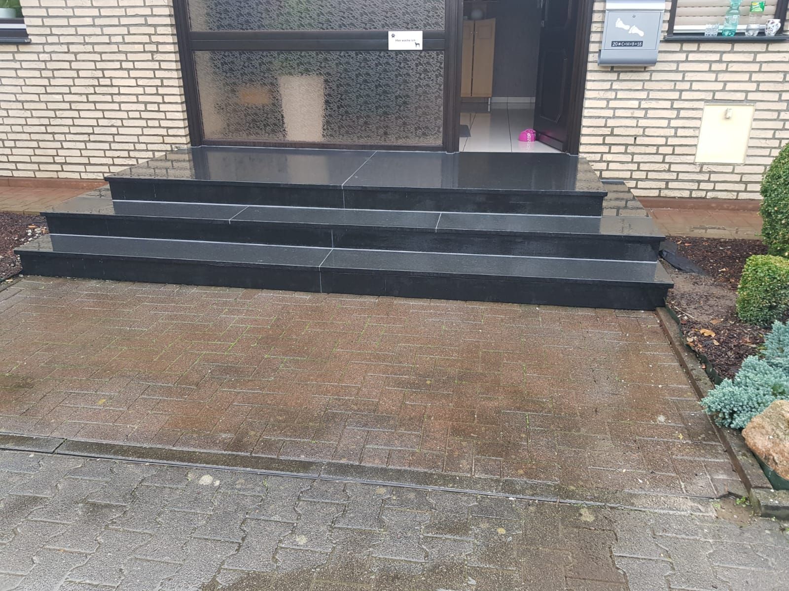 Schwarze Granitstufen führen zu einem Hauseingang mit einer Milchglastür.