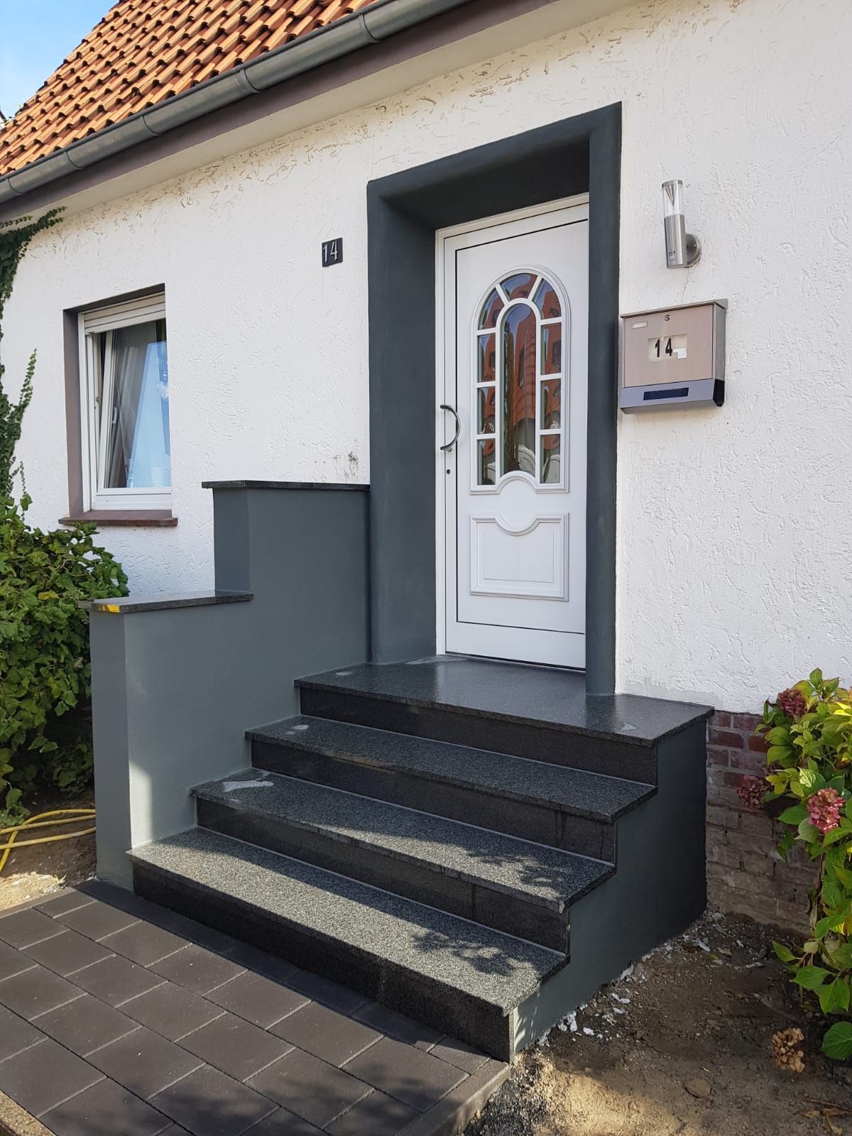 Weißer Hauseingang mit grauen Stufen und Türrahmen. Tür führt hinauf zur Haustür.