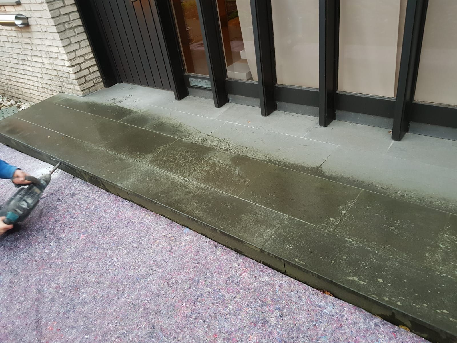 Person, die ein Elektrowerkzeug an einer rechteckigen Struktur verwendet; Gebäudeaußenseite mit sichtbarer Isolierung.