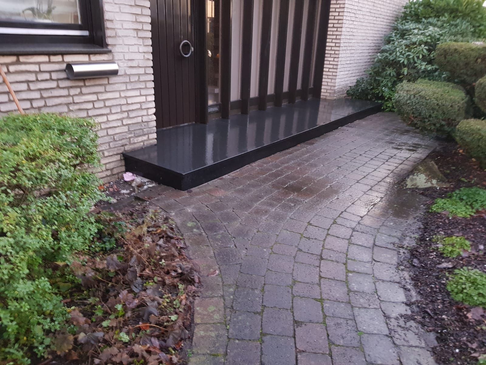 Ein Ziegelweg führt zu einer schwarzen Türplattform. Ein dunkler Ziegelweg grenzt an den Eingang.