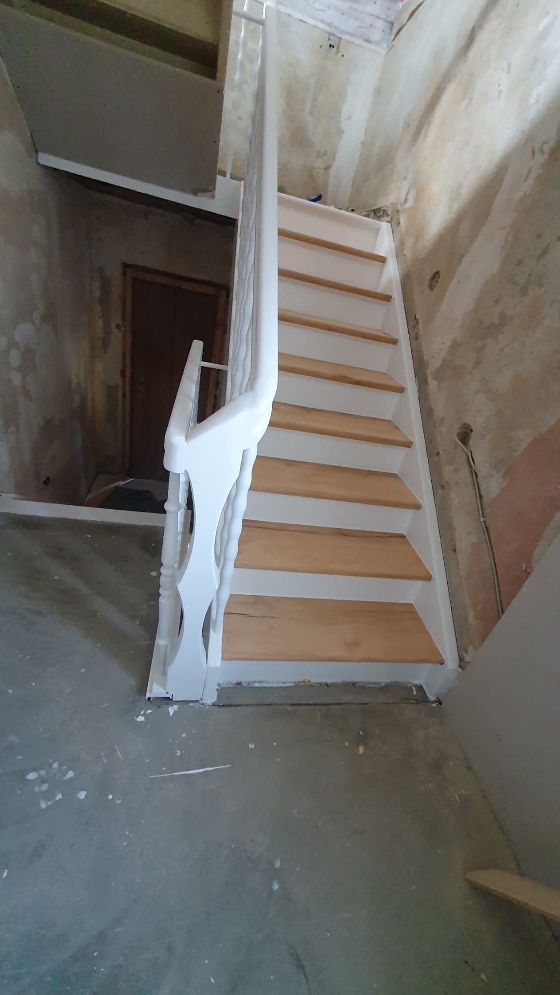 Treppe mit weißem Geländer und Holzstufen im Bau in einem Raum mit unfertigen Wänden.