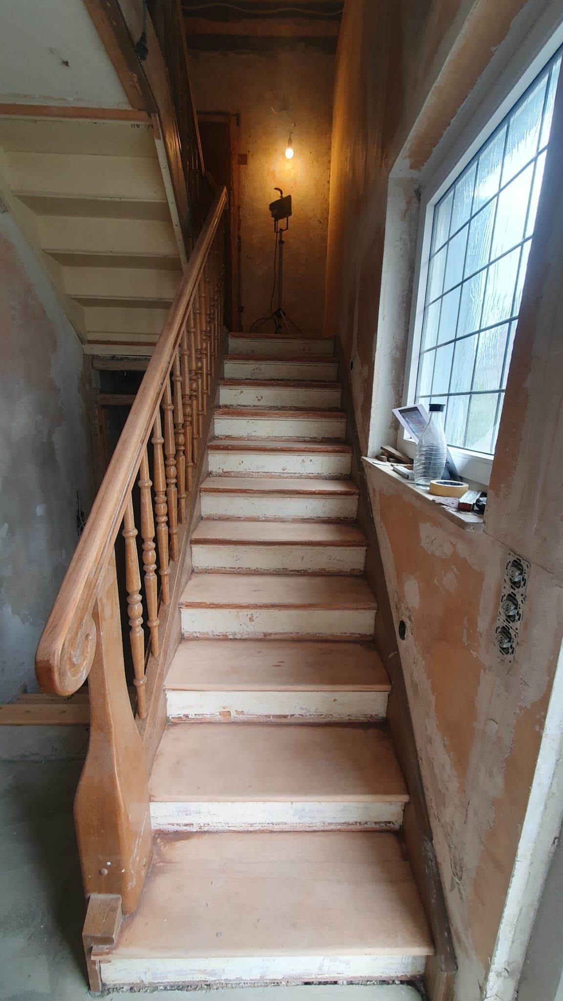Treppe mit Holzhandlauf, Licht auf dem Treppenabsatz, Fenster rechts, wird renoviert.