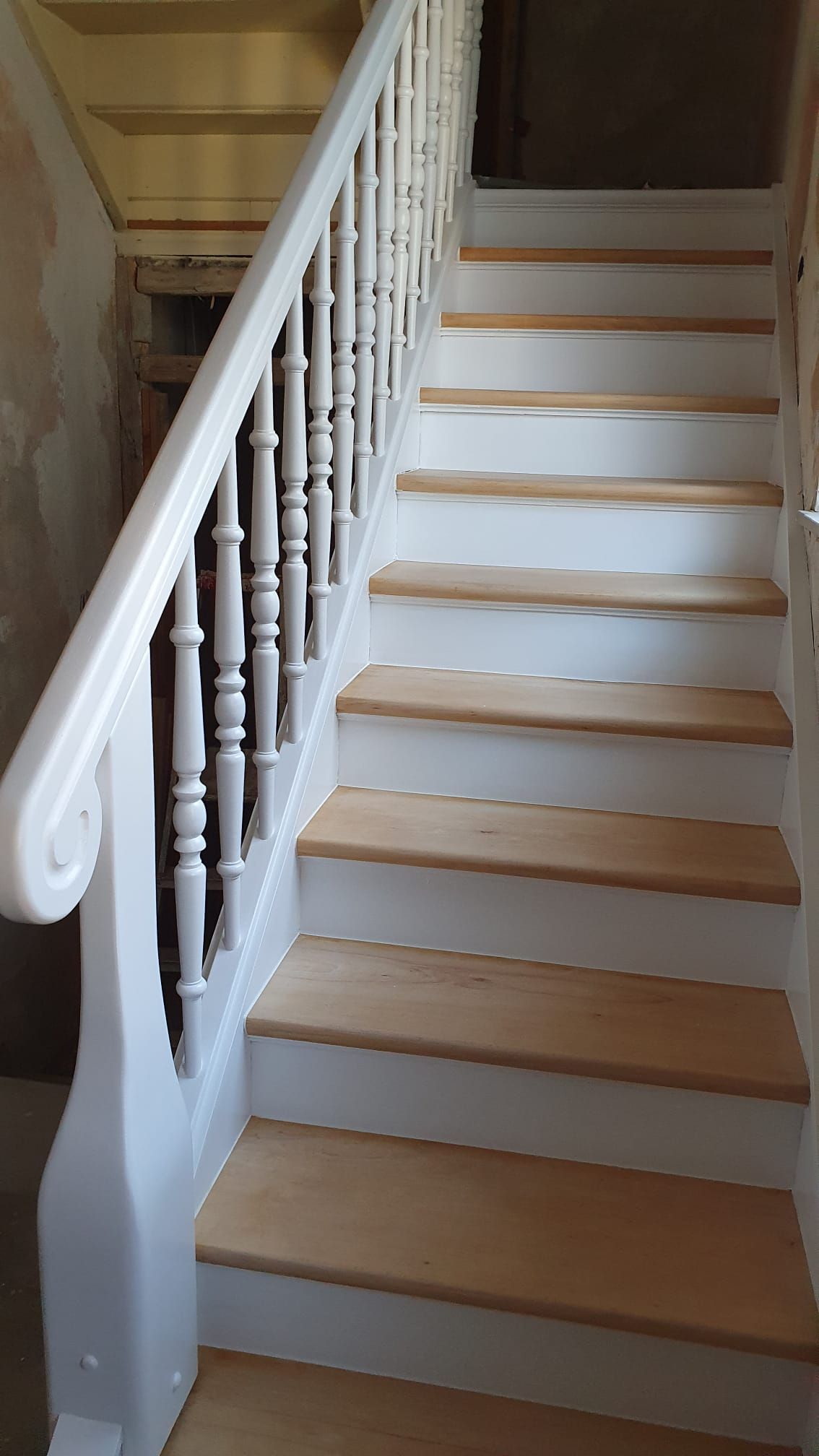 Holztreppe mit weißem Geländer und hellbraunen Stufen.