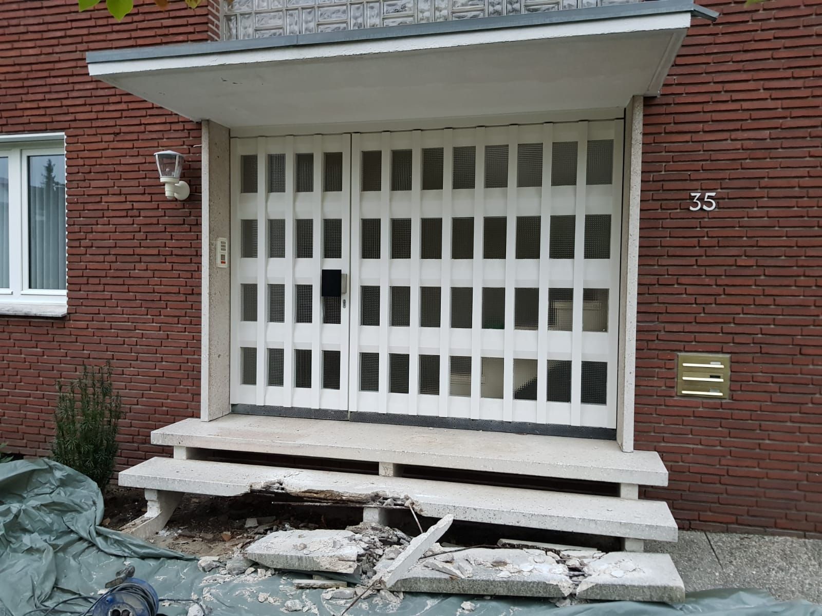 Beschädigte Betonstufen führen zu einem Gebäude mit Ziegelwänden und weißen Türen; eine Nummer 75 ist sichtbar.