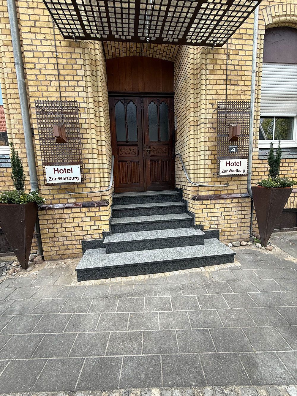 Eingang eines Gebäudes mit einer dunklen Holztür, Stufen und Schildern mit der Aufschrift „Hotel“. Ziegelfassade.