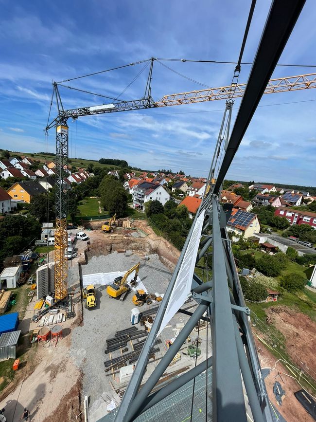 Zwei montierte Turmdrehkrane einer Kranvermietung über den Dächern eines Wohngebiets bei blauem Himmel