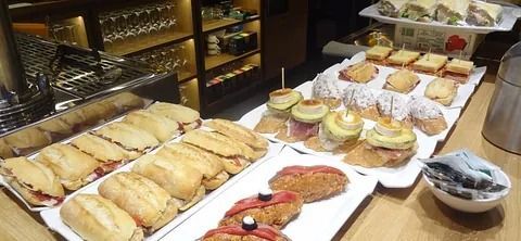 Una exhibición de varios sándwiches pequeños, tapas y pintxos en un mostrador en un bar.