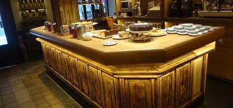 Una barra de madera de cafetería con pasteles y tazas expuestas encima.