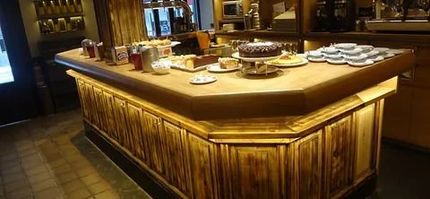 Una barra de madera de cafetería con pasteles y tazas expuestas encima.