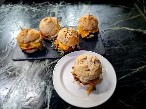 Minihamburguesas con queso en un plato y tabla de servir, con palillos. Encimera de mármol.
