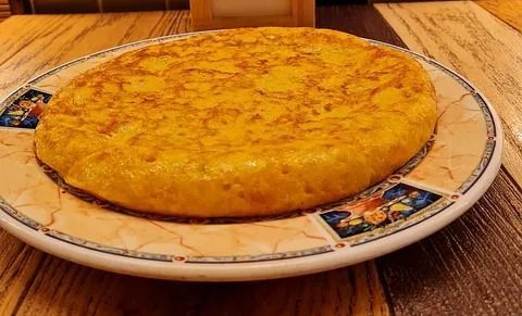 Tortilla española sobre un plato decorativo en una mesa de madera.