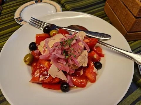 Ensalada con tomates, aceitunas y atún, cubierta con cebolla roja en un plato blanco con cubiertos.