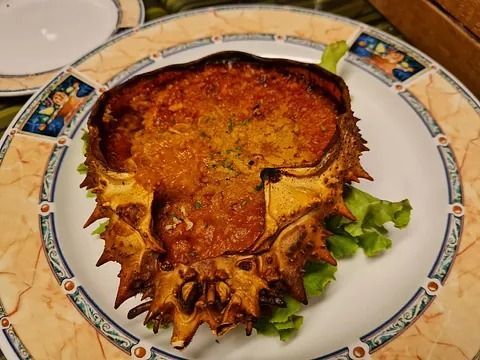 Plato de cangrejo al horno en su caparazón, servido sobre lechuga en un plato decorado.