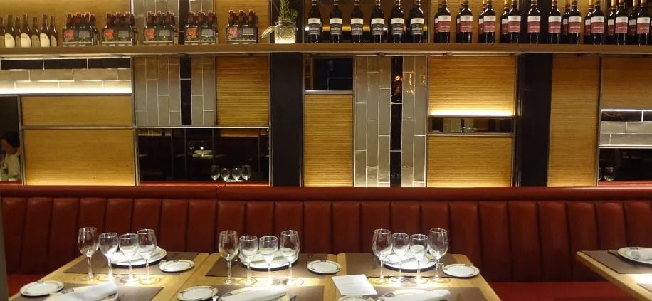 Interior del restaurante: mesas preparadas con vasos y platos, cabinas rojas, estantes con botellas de vino.