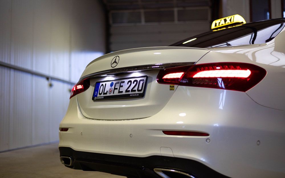 Ein weißer Mercedes Benz mit einem Taxischild auf dem Dach steht in einer Garage.