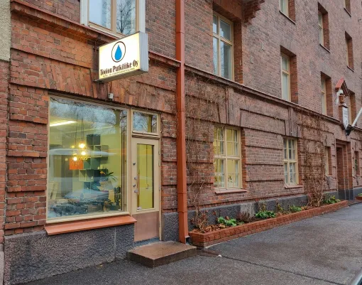Tiilinen liiketila, jossa on suuret ikkunat ja valaistu kyltti märällä kadunkulmalla.