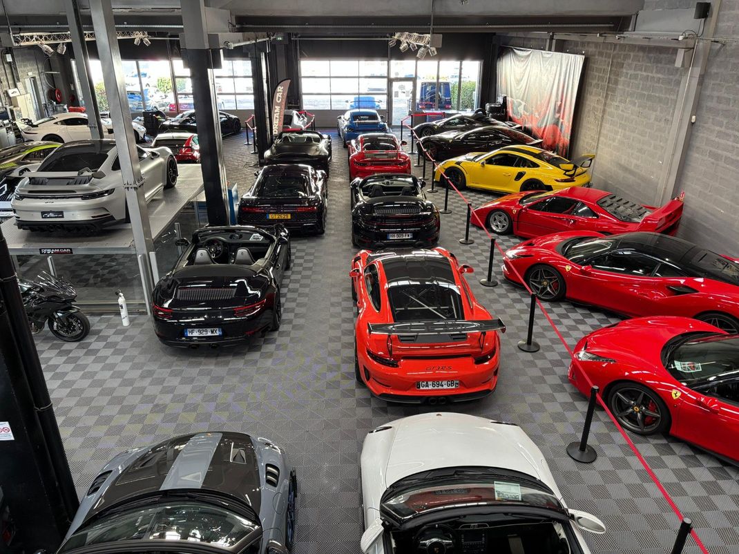 Salle d'exposition de voitures de luxe remplie de voitures de sport, notamment des véhicules rouges, noirs, blancs et jaunes.