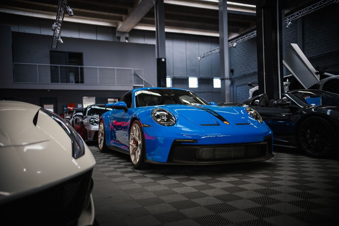 Une voiture de sport bleue exposée dans un showroom, flanquée d'autres voitures de luxe.