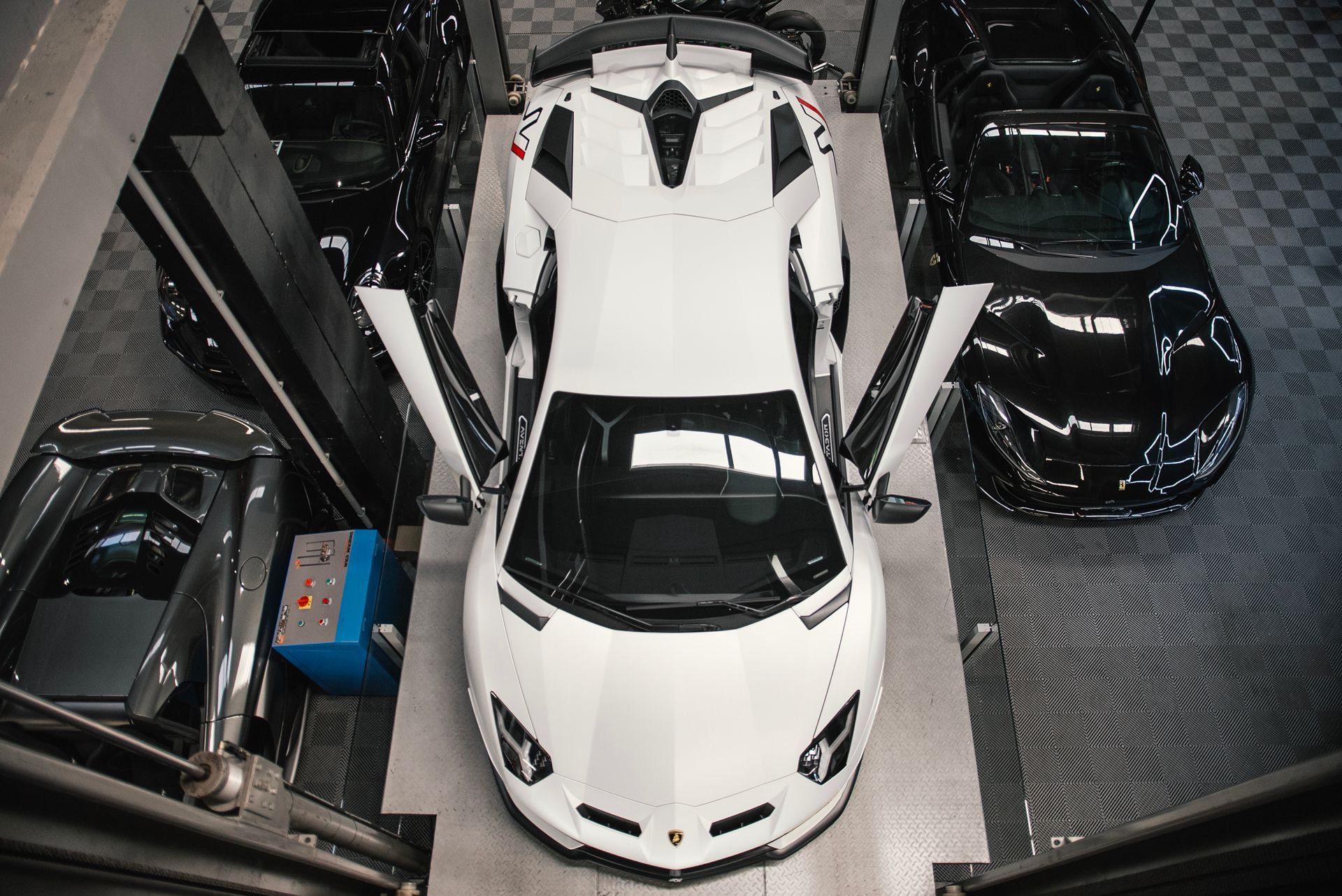 Vue aérienne d'une voiture de sport blanche garée serrée entre plusieurs voitures noires dans un garage 