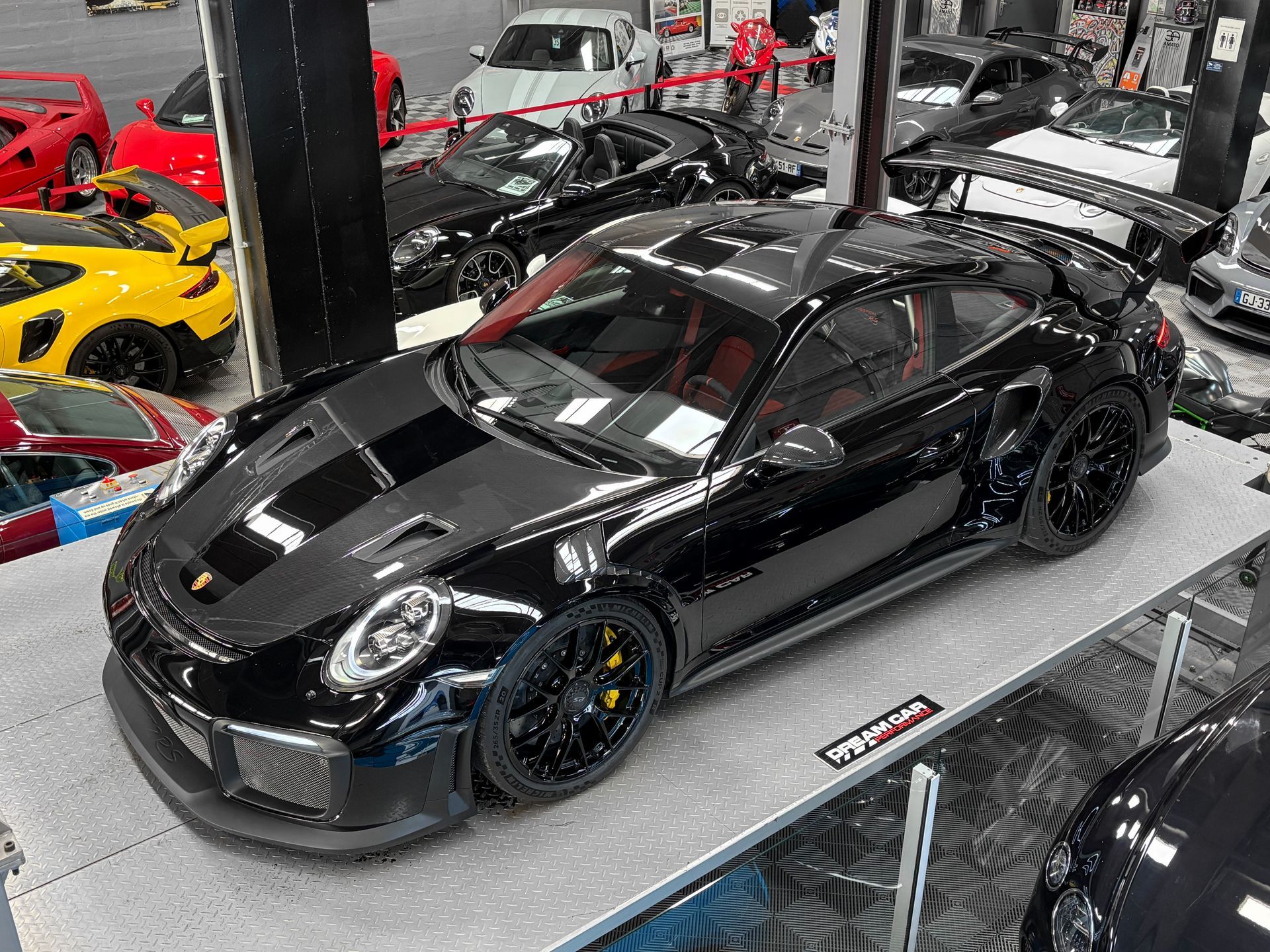 Une Porsche 911 noire exposée dans un showroom automobile, entourée d'autres voitures de sport.
