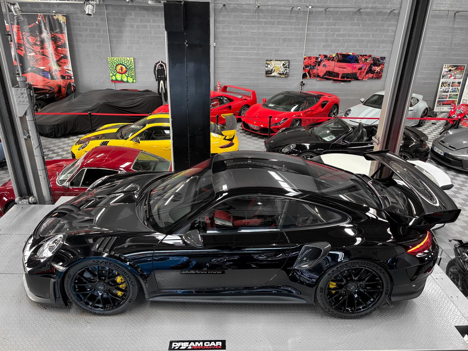 Une Porsche 911 noire exposée dans un showroom automobile, entourée d'autres voitures de sport.