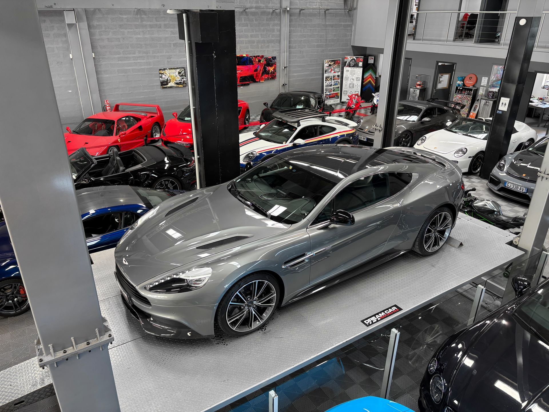 Voiture de sport argentée dans un showroom, entourée d'autres voitures exotiques.