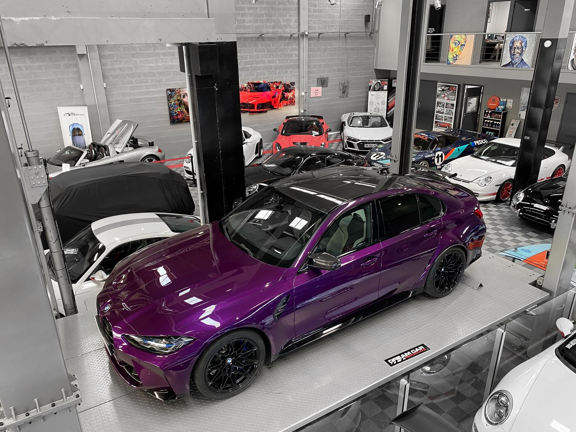 Une berline sport violette dans un garage, entourée d'autres voitures et d'équipements sur un pont élévateur.