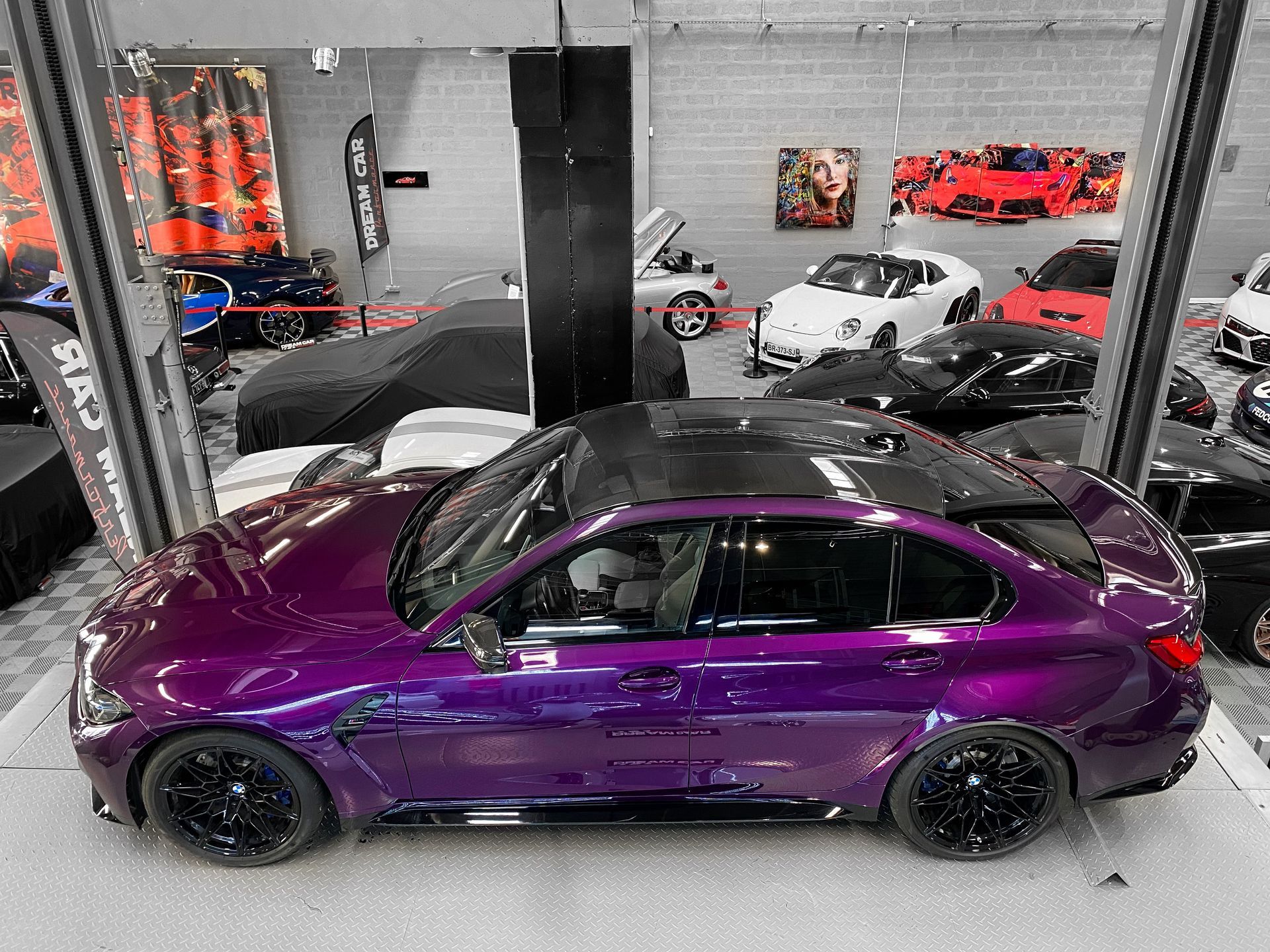 Une berline sport violette dans un garage, entourée d'autres voitures et d'équipements sur un pont élévateur.