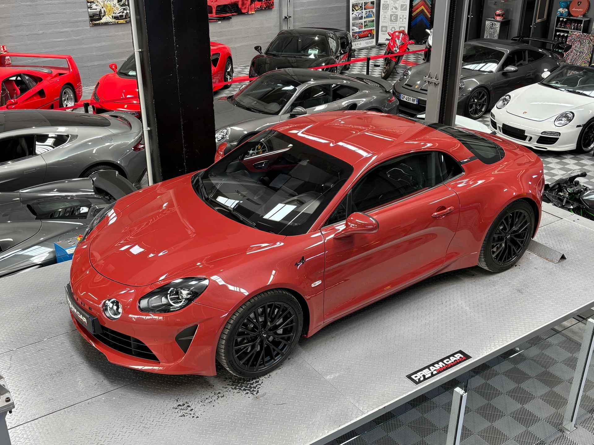 Un coupé Mercedes rouge exposé dans un showroom, avec d'autres voitures de sport en arrière-plan.