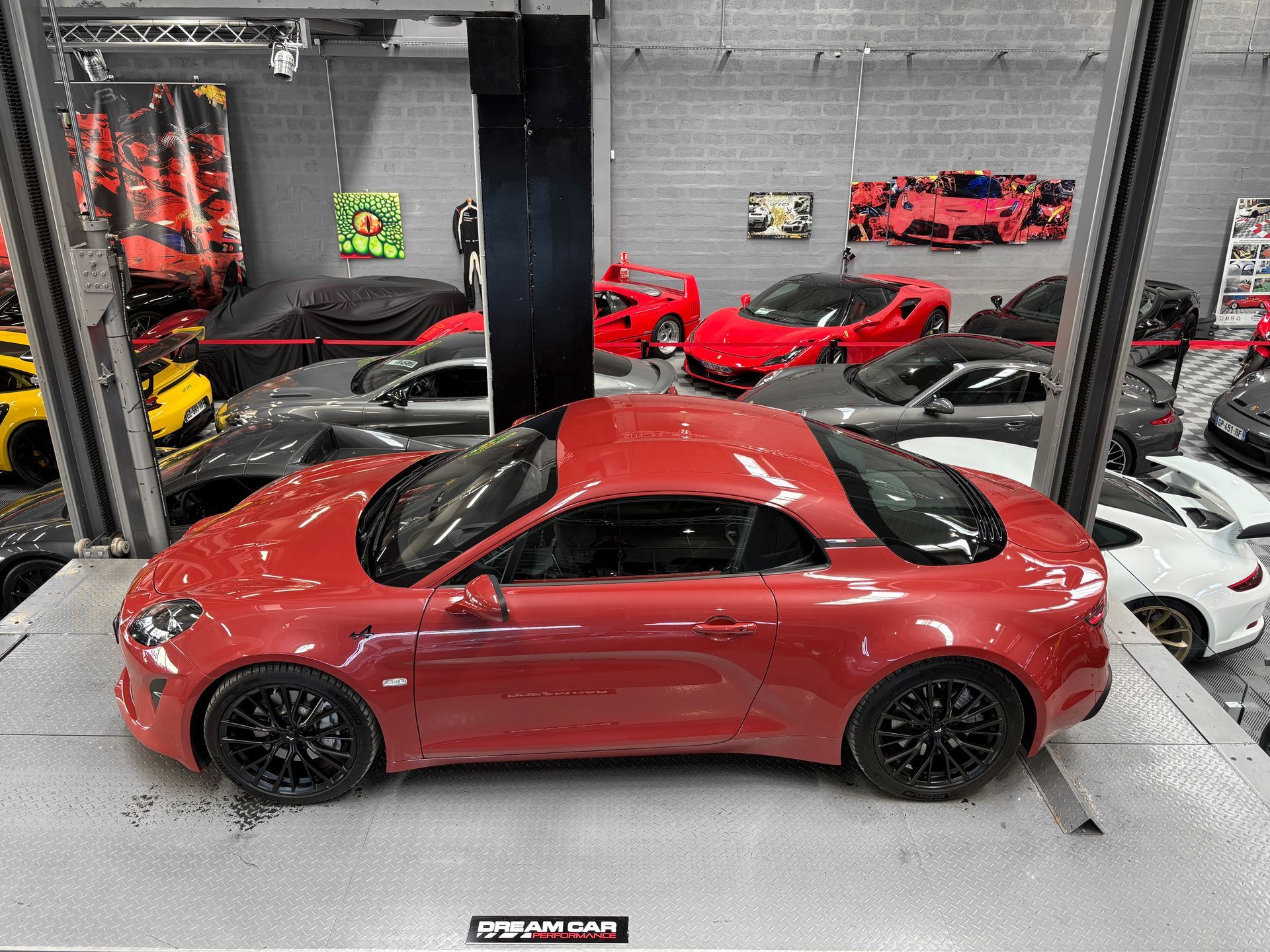 Un coupé Mercedes rouge exposé dans un showroom, avec d'autres voitures de sport en arrière-plan.