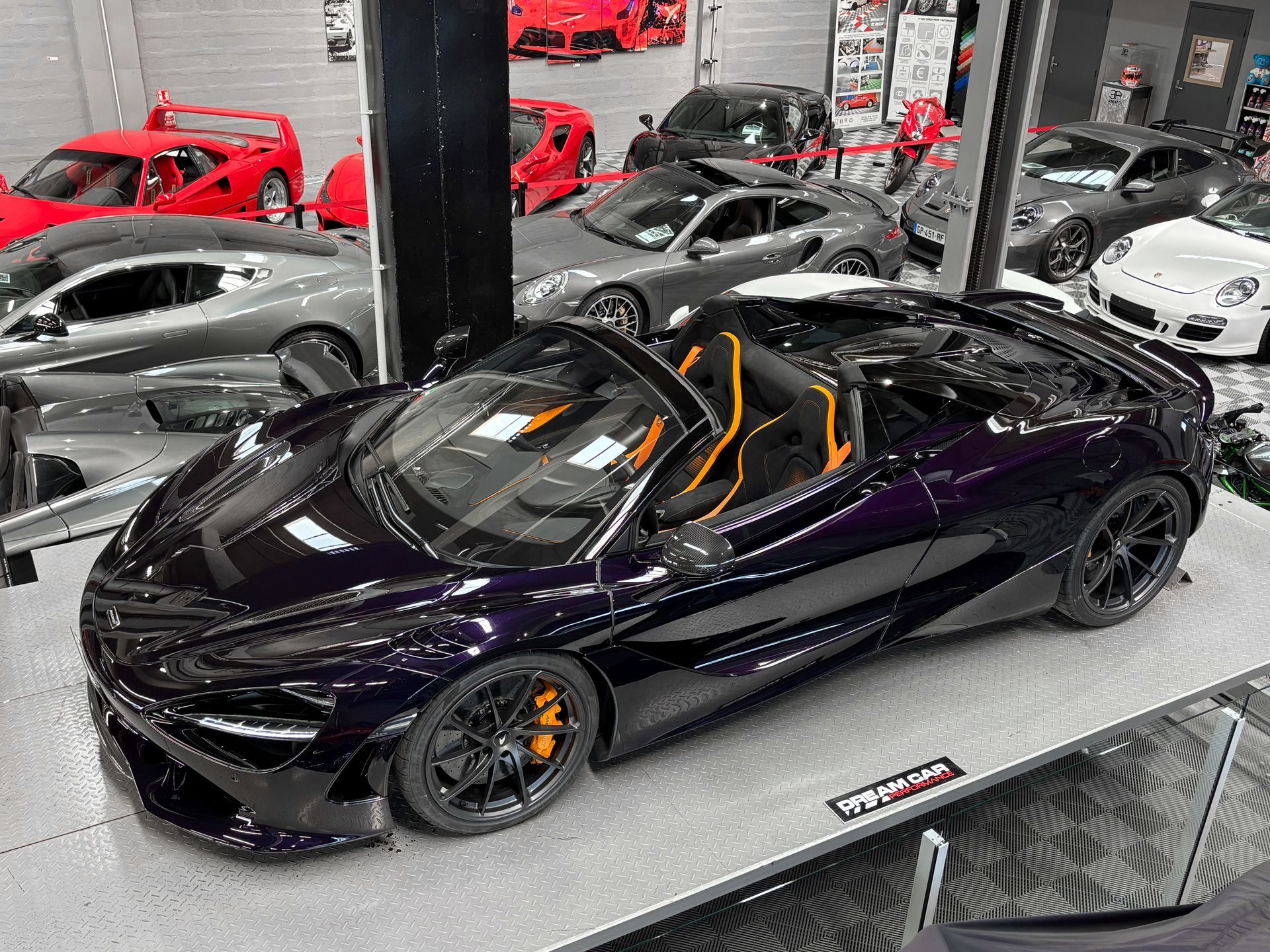 Voiture de sport violette brillante avec des accents orange exposée dans une salle d'exposition parmi d'autres voitures