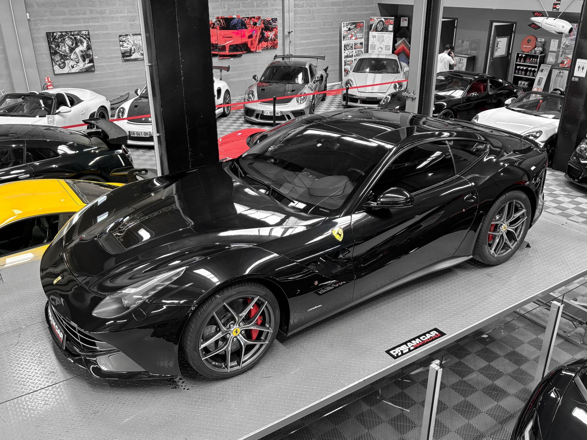 Une Ferrari noire est exposée à l'intérieur d'un showroom automobile, avec d'autres véhicules en arrière-plan.