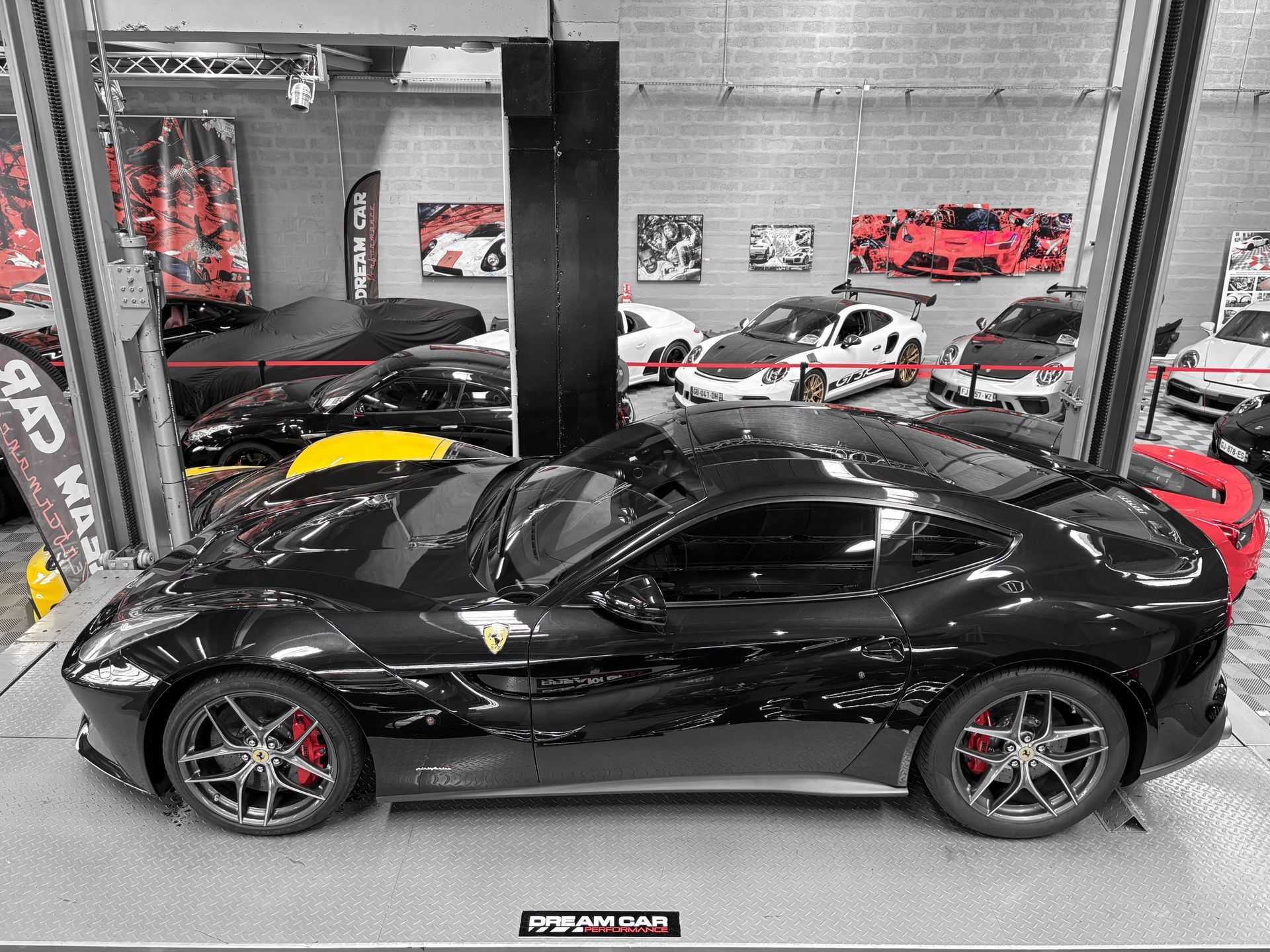 Une Ferrari noire est exposée à l'intérieur d'un showroom automobile, avec d'autres véhicules en arrière-plan.