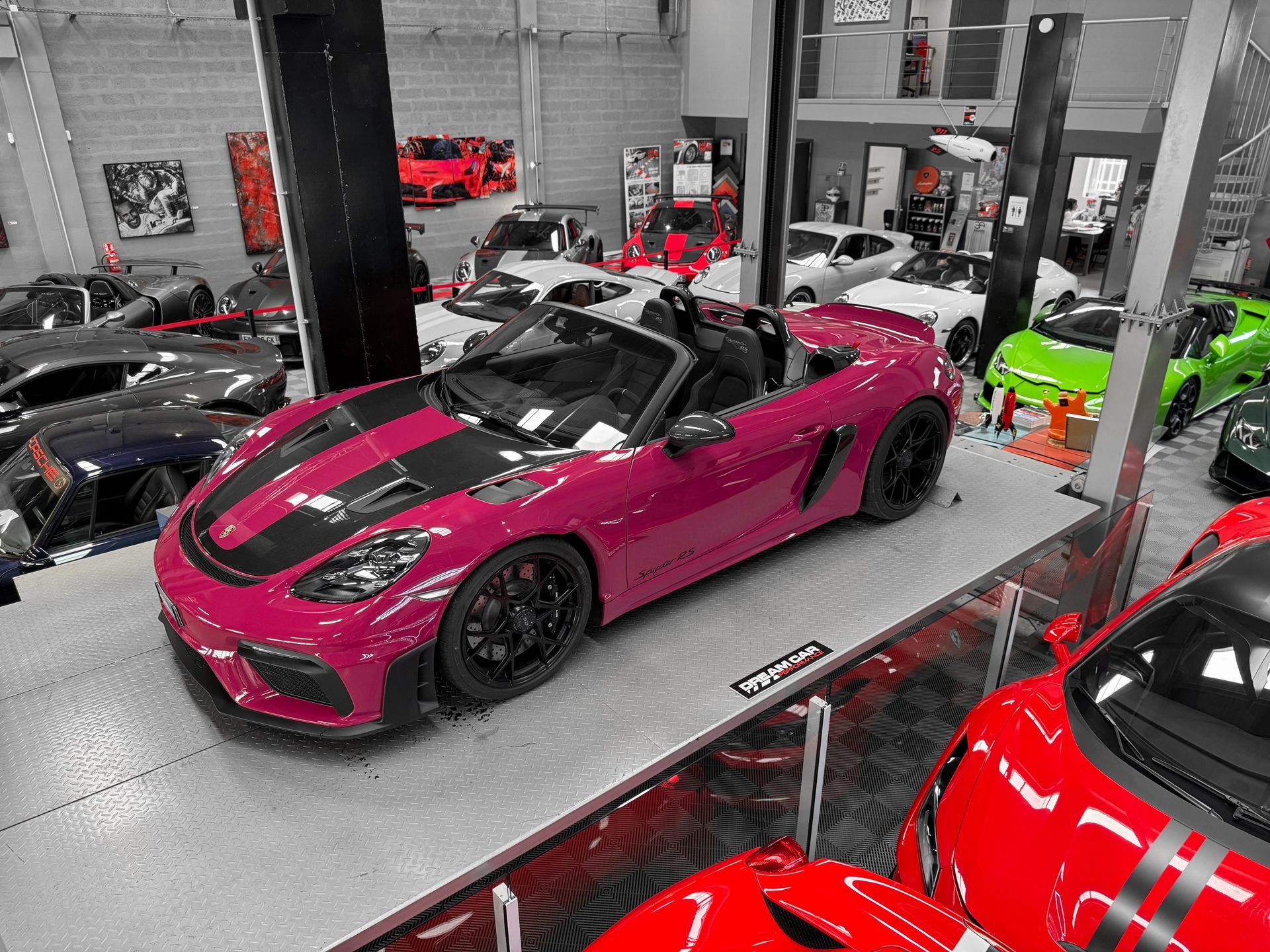 Une voiture de sport magenta exposée sur un plateau tournant dans un showroom, parmi d'autres voitures performantes.