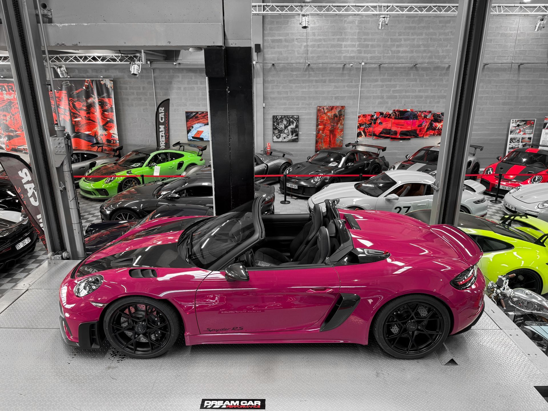 Une voiture de sport magenta exposée sur un plateau tournant dans un showroom, parmi d'autres voitures performantes.