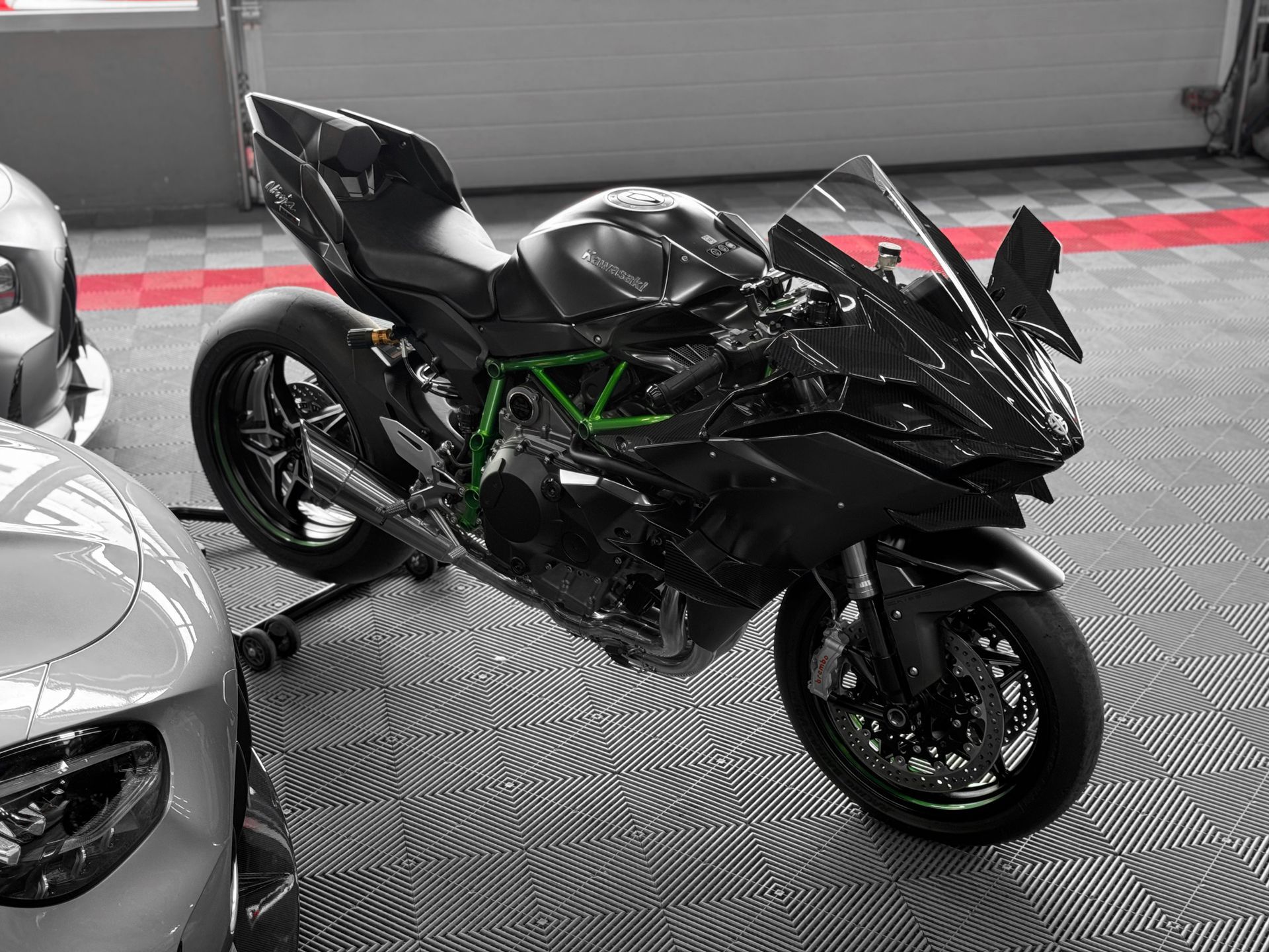 Une moto sport noire exposée dans un showroom entre deux voitures sport argentées