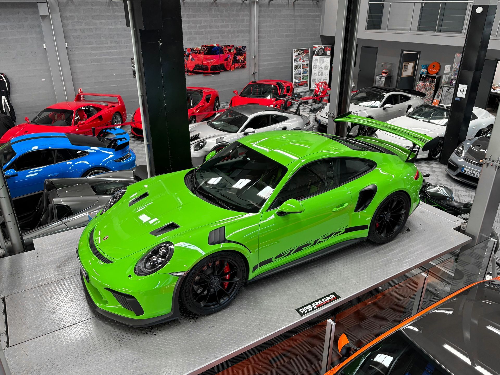 Voiture de sport vert vif dans une salle d'exposition, entourée de plusieurs voitures rouges, bleues et blanches