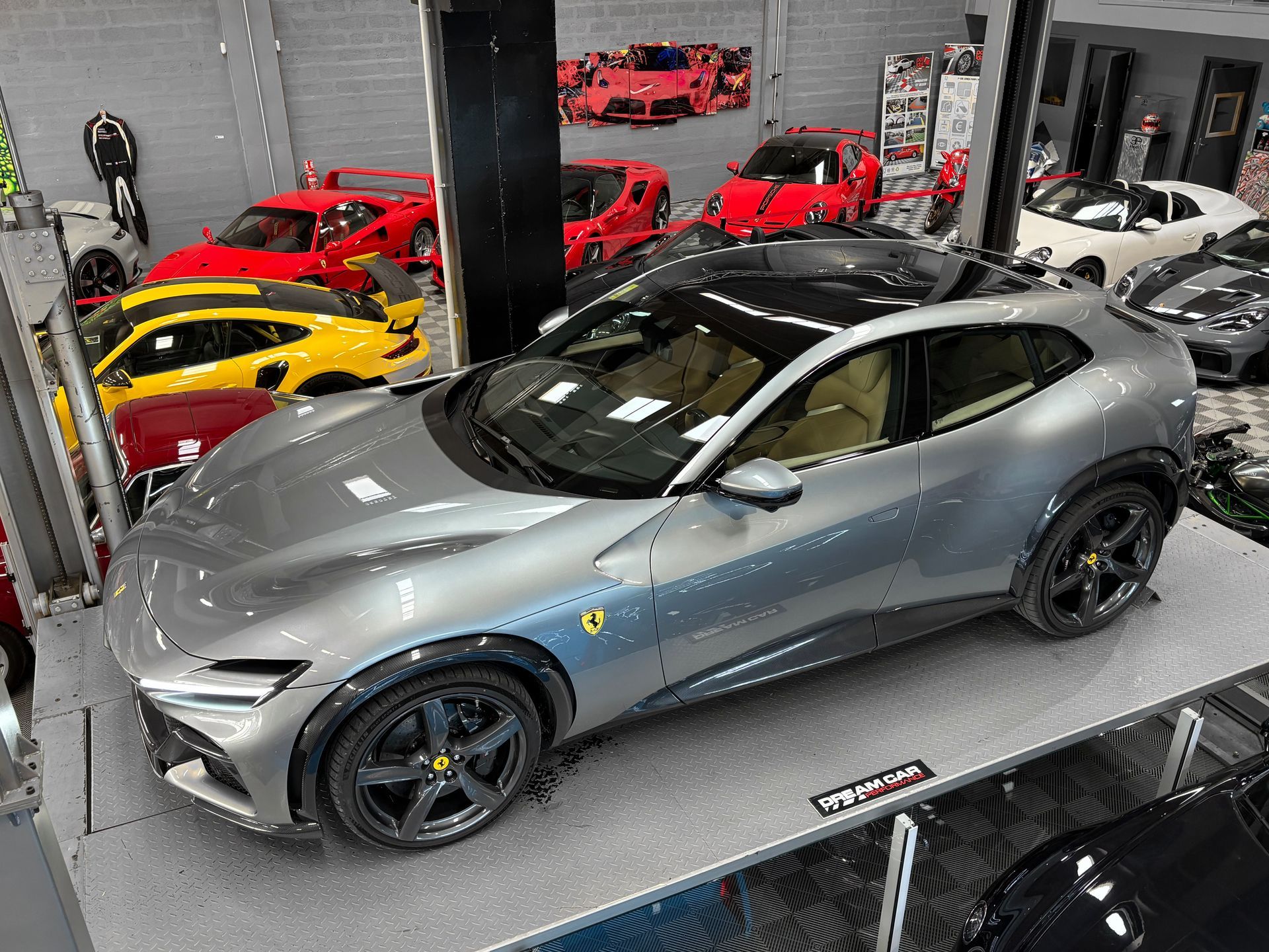 Un SUV Ferrari argenté dans un showroom avec des voitures de sport rouges et jaunes en arrière-plan.