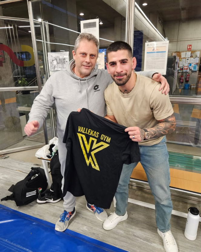 Dos hombres de pie uno al lado del otro sosteniendo una camiseta que dice gimnasio de bienestar.