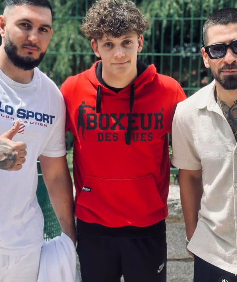 Tres hombres posan para una foto, uno de ellos lleva una sudadera roja con capucha que dice 