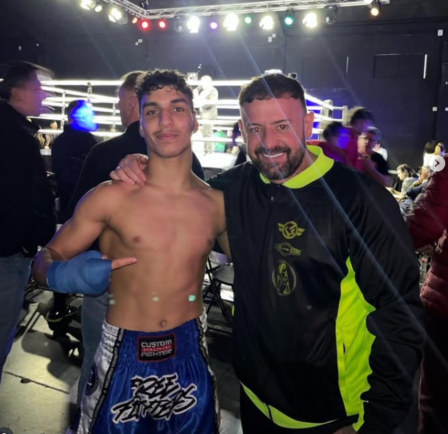 Dos hombres posan para una foto en un ring de boxeo y uno de ellos lleva pantalones cortos de boxeo.