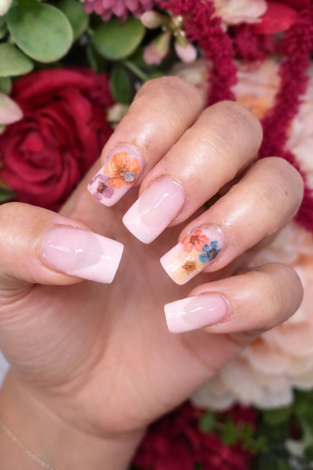 Main avec des ongles rose pâle et des ongles décorés de motifs floraux sur fond de bouquet