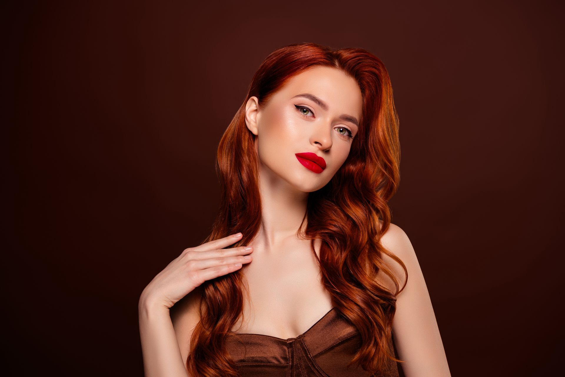 Portrait d'une femme rousse au rouge à lèvres rouge, posant sur un fond brun foncé