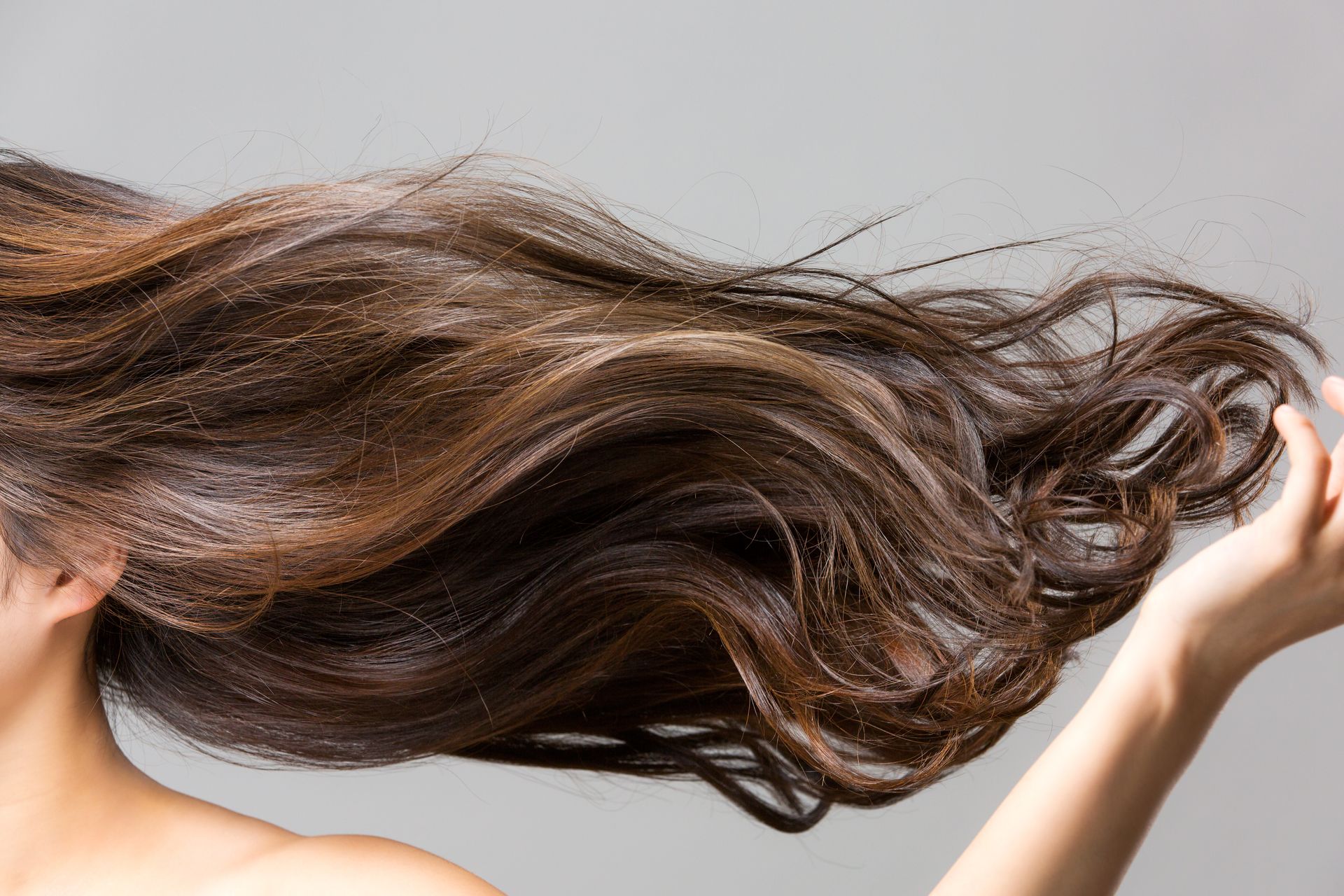 Femme faisant tournoyer ses longs cheveux bruns sur un fond gris clair
