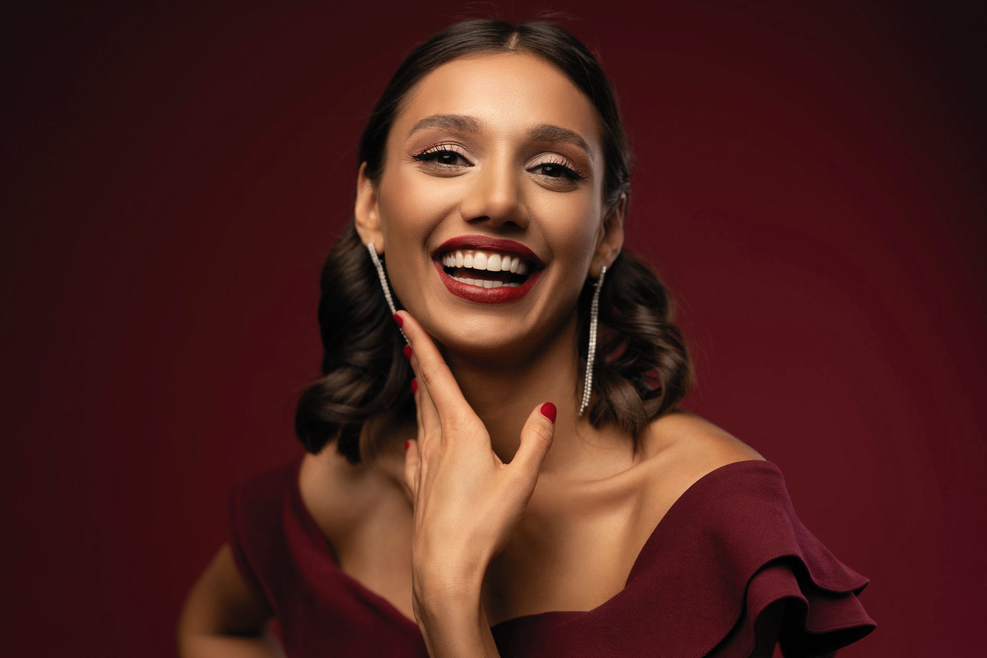 Portrait d'une femme souriante en robe bordeaux sur fond rouge foncé
