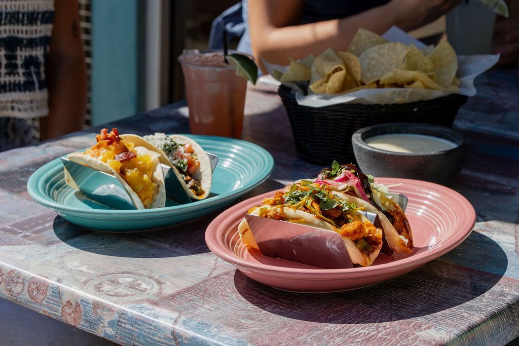 Tacos on colorful plates, chips, salsa, and a drink on an outdoor table.