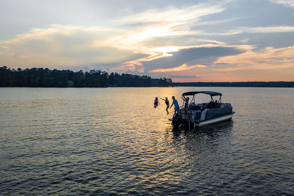 Pontoon boat on a lake at sunset; two people in the water, one on the boat.