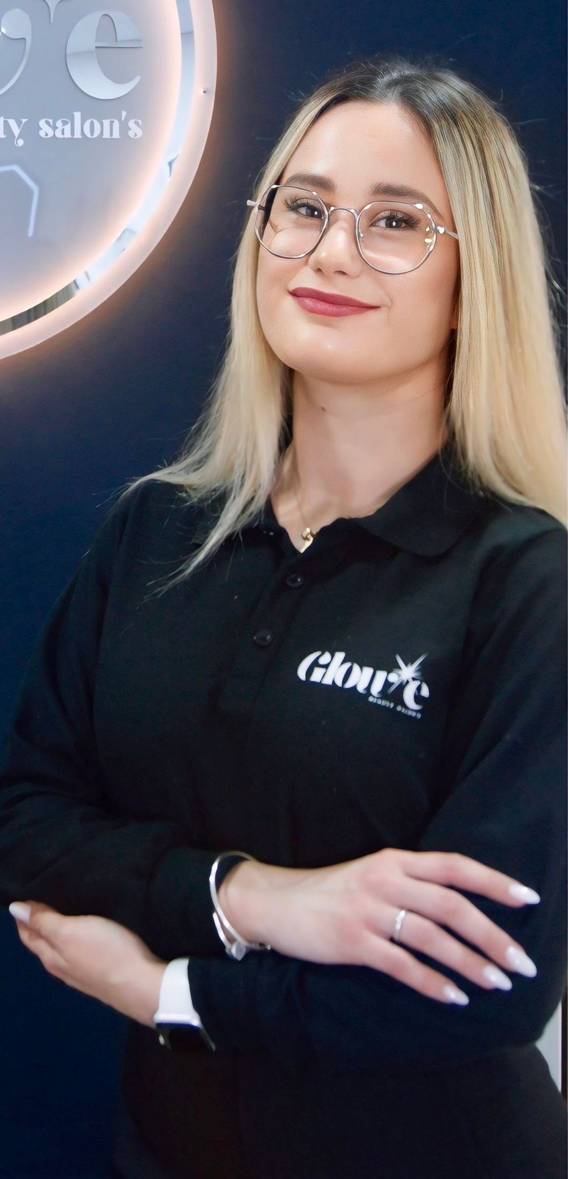 Una mujer que lleva gafas y un polo negro está de pie con los brazos cruzados.