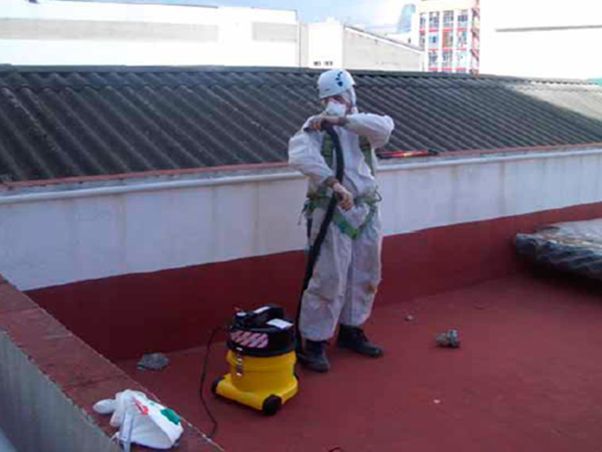 Un hombre con un traje de protección está de pie en un tejado con una aspiradora.