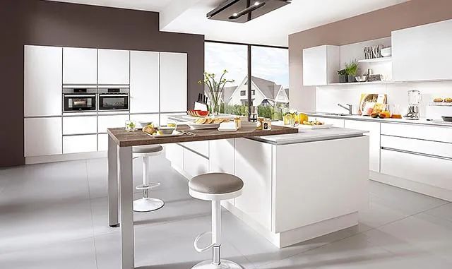 Una cocina con muebles blancos y una gran isla con mesa y taburetes.